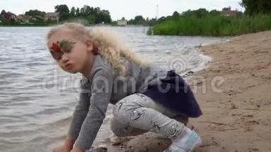 四岁的贪玩女孩坐在湖水边用沙子付钱。 万向节运动